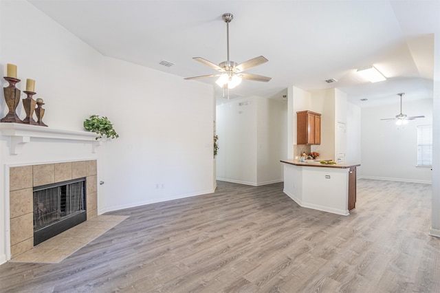 unfurnished living room featuring light wood-style flooring, a tile fireplace, visible vents, and a ceiling fan