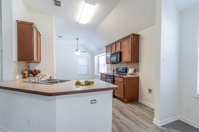 kitchen with visible vents, brown cabinetry, lofted ceiling, black appliances, and a sink