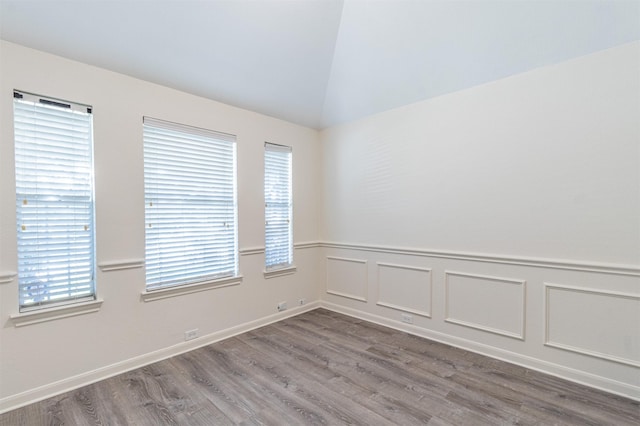 empty room with lofted ceiling, a wainscoted wall, a decorative wall, and wood finished floors