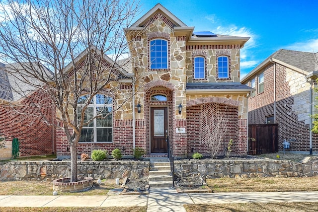 view of front of house with stone siding, fence, solar panels, and brick siding