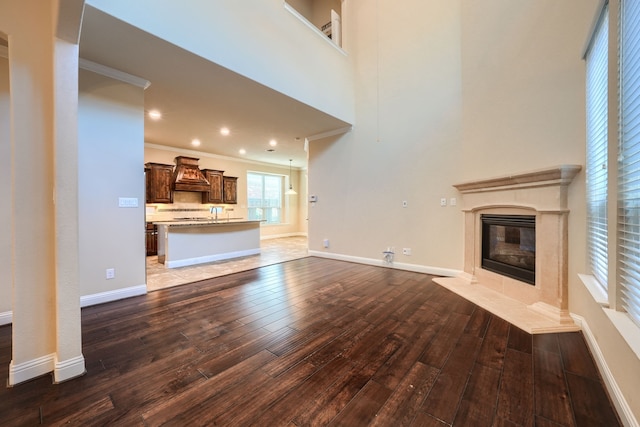 unfurnished living room featuring a towering ceiling, a premium fireplace, ornamental molding, baseboards, and hardwood / wood-style flooring