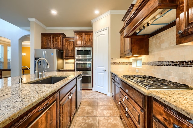 kitchen featuring light stone counters, stainless steel appliances, premium range hood, a sink, and crown molding