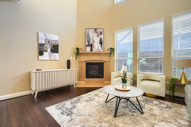 sitting room with baseboards, a glass covered fireplace, a towering ceiling, hardwood / wood-style flooring, and radiator heating unit