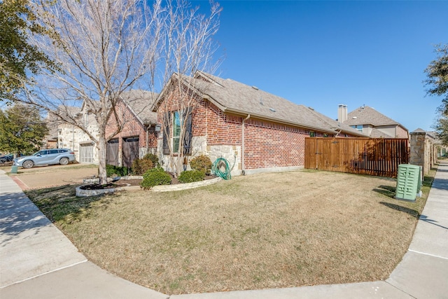 view of side of home with roof with shingles, brick siding, a yard, fence, and stone siding