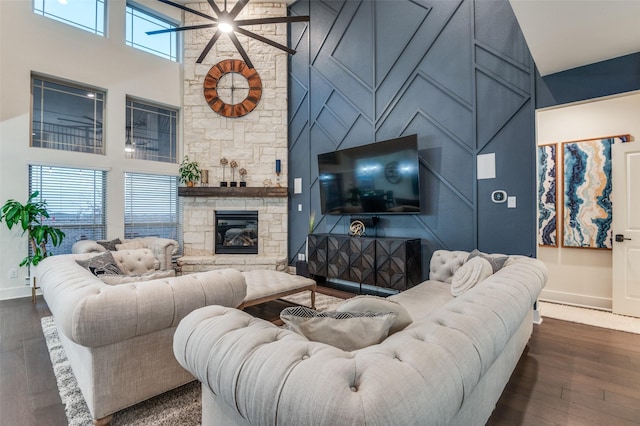 living area with baseboards, a towering ceiling, an accent wall, dark wood-style flooring, and a fireplace