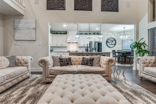 living room featuring baseboards, a high ceiling, a chandelier, and wood finished floors