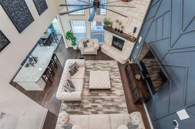 living area featuring a fireplace, a towering ceiling, baseboards, and wood finished floors