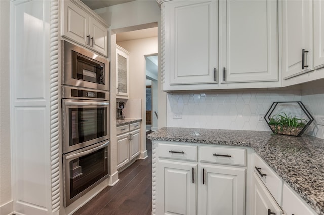 kitchen featuring stone counters, dark wood-style flooring, stainless steel microwave, decorative backsplash, and white cabinets