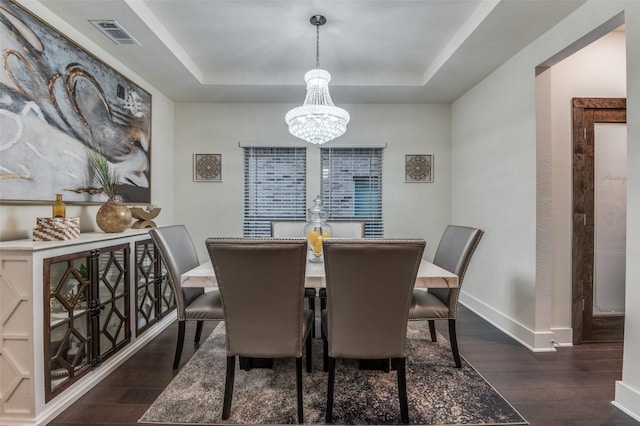 dining area with visible vents, dark wood finished floors, baseboards, a tray ceiling, and a chandelier