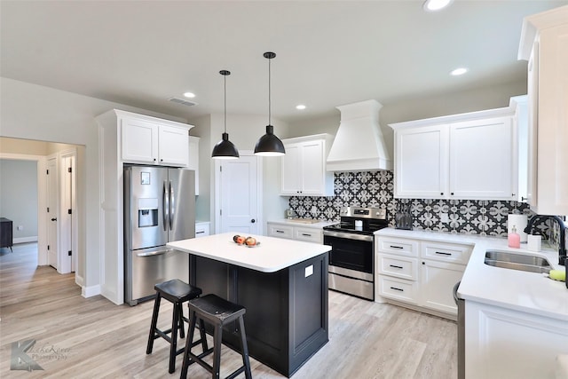 kitchen with visible vents, appliances with stainless steel finishes, a sink, a kitchen island, and premium range hood