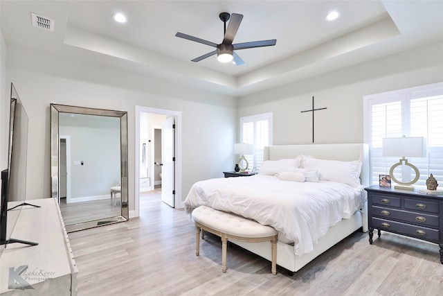 bedroom with a raised ceiling, visible vents, light wood-style flooring, and baseboards