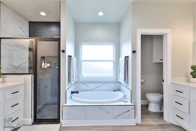 bathroom featuring toilet, a garden tub, a shower stall, and wood finished floors