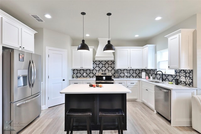 kitchen featuring tasteful backsplash, light countertops, custom range hood, appliances with stainless steel finishes, and a sink