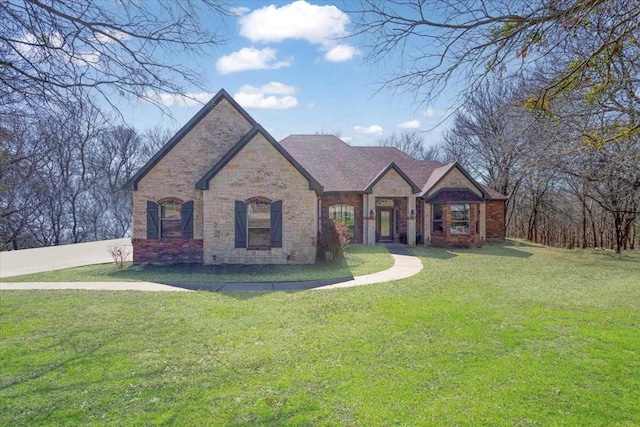 french provincial home featuring brick siding, roof with shingles, and a front yard