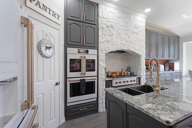 kitchen featuring white appliances, light stone counters, a kitchen island with sink, a sink, and gray cabinetry