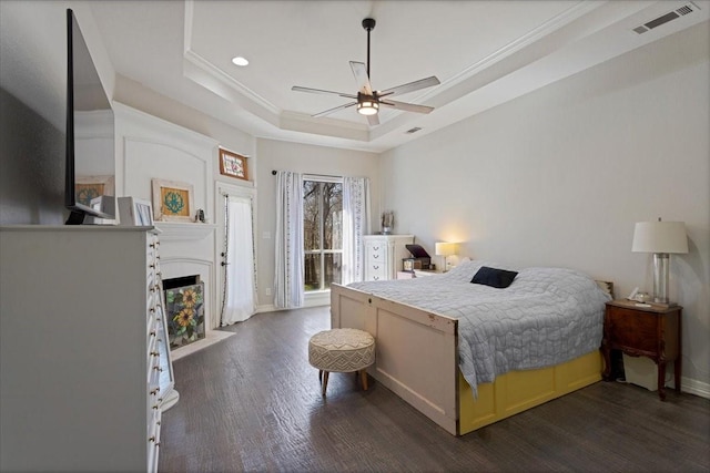 bedroom with visible vents, a fireplace with flush hearth, ornamental molding, a tray ceiling, and dark wood-style flooring