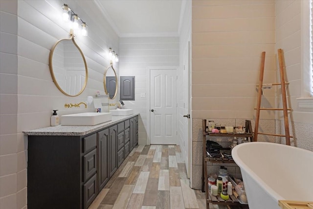 full bathroom with a freestanding bath, double vanity, wood finished floors, and a sink