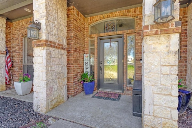 doorway to property featuring brick siding, stone siding, and covered porch