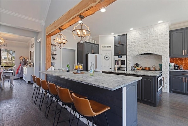 kitchen featuring a notable chandelier, high end fridge, ornamental molding, a kitchen breakfast bar, and a center island