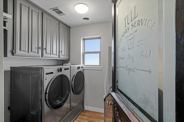 laundry room with cabinet space, visible vents, light wood finished floors, and washer and dryer