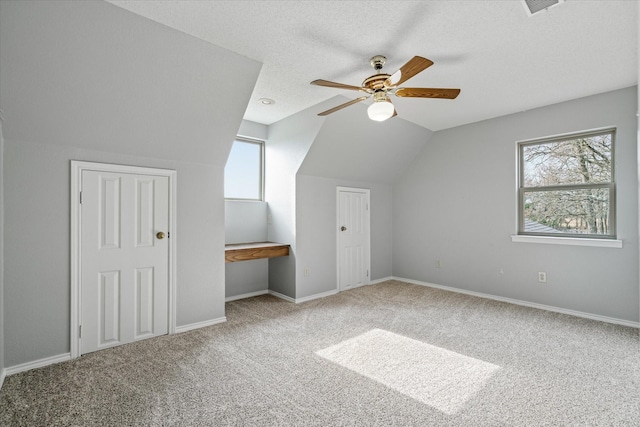 bonus room with a ceiling fan, carpet, vaulted ceiling, a textured ceiling, and built in desk