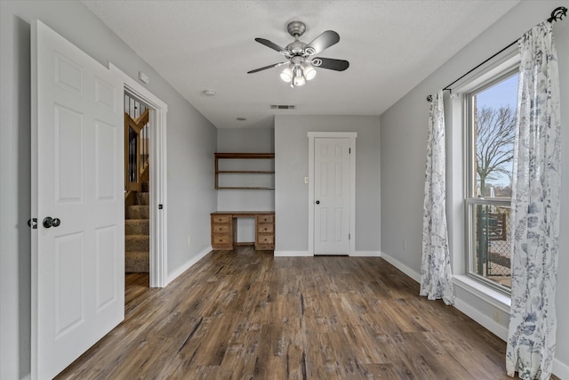 unfurnished bedroom with visible vents, built in desk, baseboards, and wood finished floors