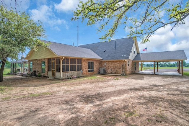 back of property featuring a carport, central AC, brick siding, and dirt driveway