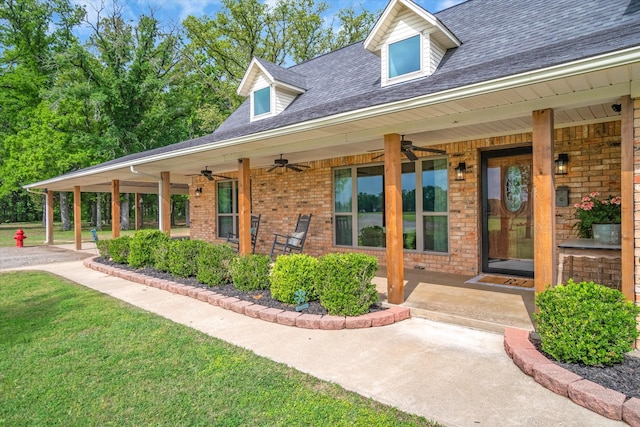 doorway to property with ceiling fan, brick siding, a lawn, and a shingled roof