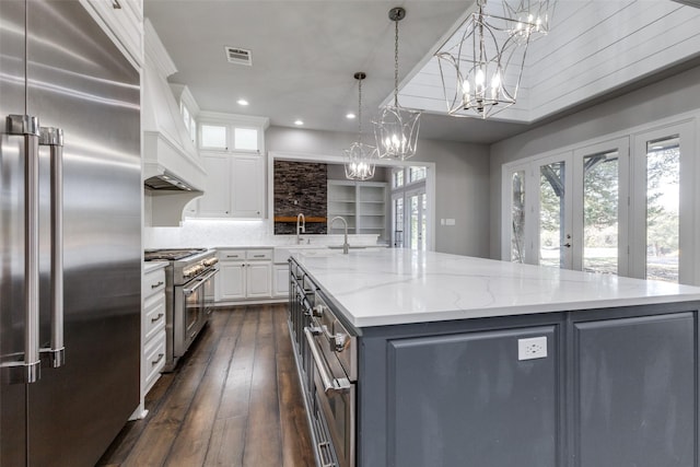 kitchen with premium appliances, light stone counters, visible vents, white cabinetry, and a large island with sink