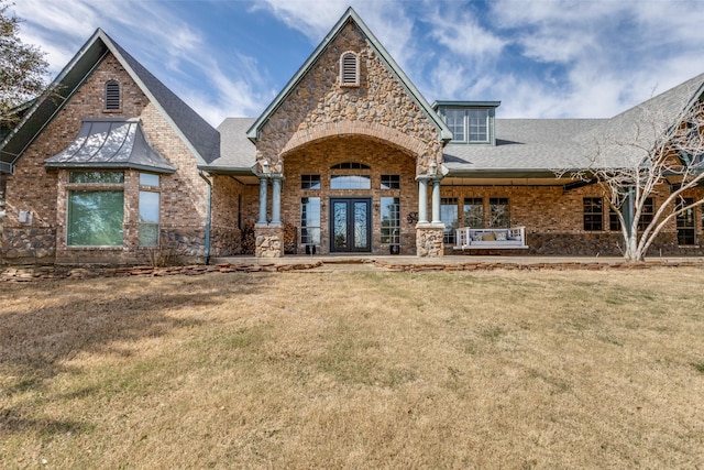 view of front facade with brick siding, a shingled roof, stone siding, french doors, and a front yard