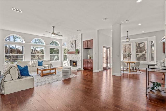 living room featuring a brick fireplace, dark wood-style floors, visible vents, and recessed lighting