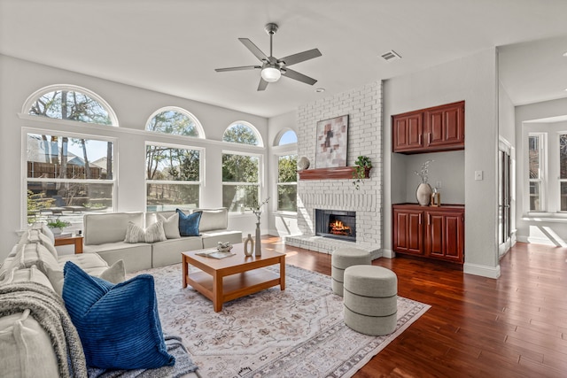 living room with baseboards, visible vents, dark wood finished floors, ceiling fan, and a fireplace