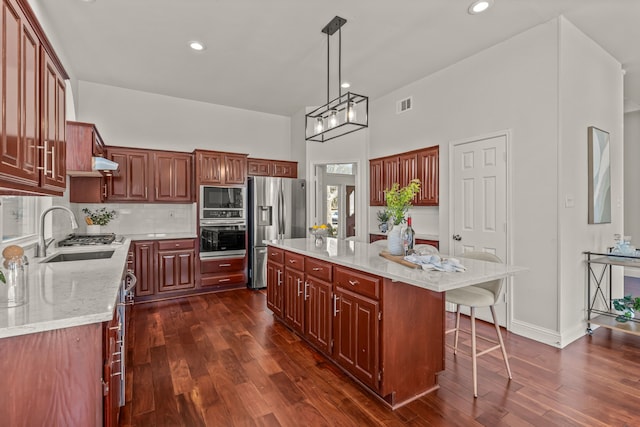 kitchen with a breakfast bar area, a kitchen island, a sink, appliances with stainless steel finishes, and decorative backsplash