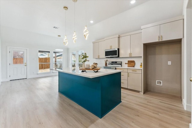 kitchen with light countertops, appliances with stainless steel finishes, a center island, light wood finished floors, and decorative light fixtures