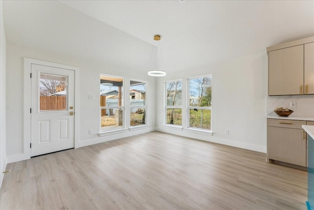 unfurnished dining area with lofted ceiling, light wood-style flooring, and baseboards