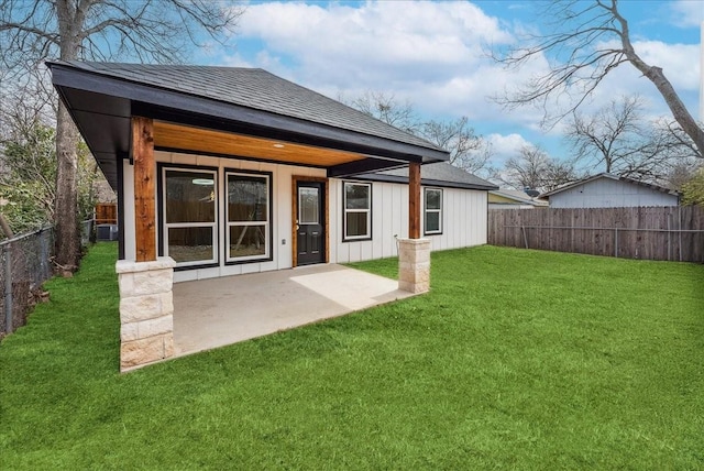 rear view of house with a yard, a patio, a shingled roof, board and batten siding, and a fenced backyard