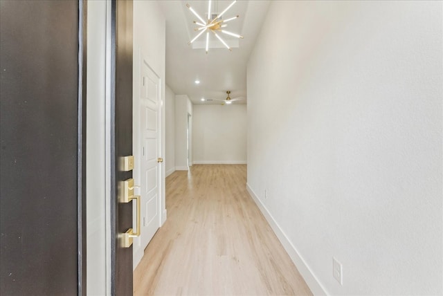 corridor featuring baseboards, a chandelier, and light wood-style floors