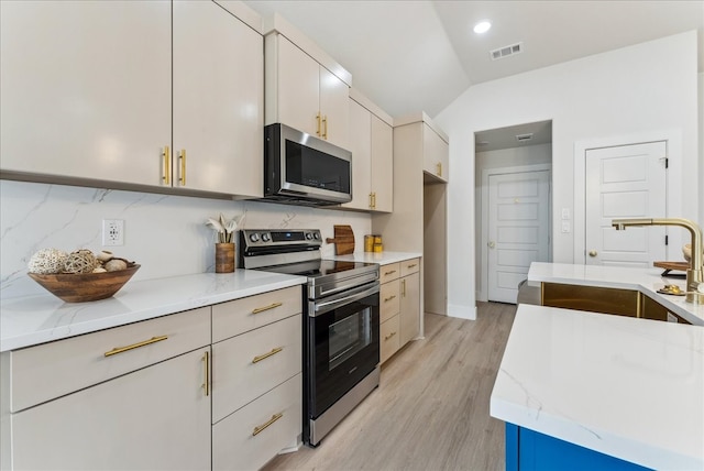 kitchen featuring visible vents, vaulted ceiling, stainless steel appliances, light wood-type flooring, and a sink