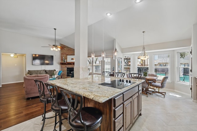 kitchen featuring lofted ceiling, black electric cooktop, a kitchen breakfast bar, a fireplace, and a ceiling fan