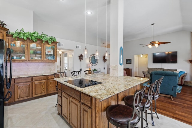 kitchen with visible vents, black appliances, light stone counters, a kitchen breakfast bar, and brown cabinetry