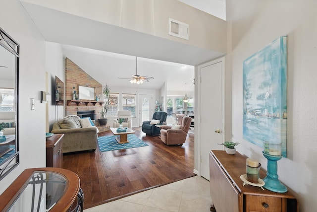 living area with visible vents, ceiling fan, a fireplace, light tile patterned flooring, and high vaulted ceiling