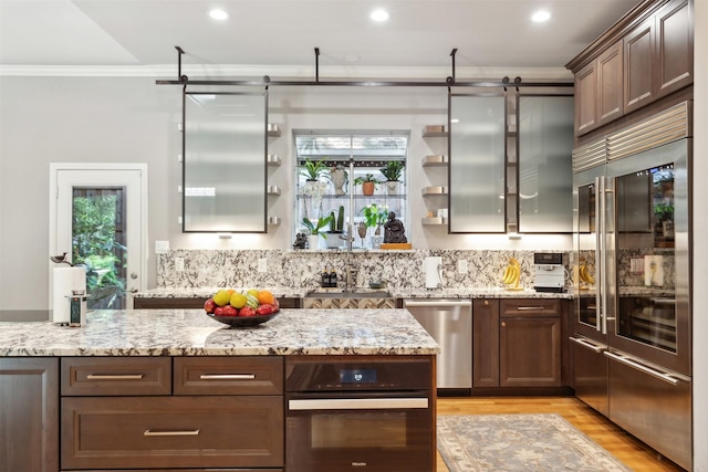 kitchen featuring light stone counters, crown molding, light wood finished floors, open shelves, and stainless steel appliances