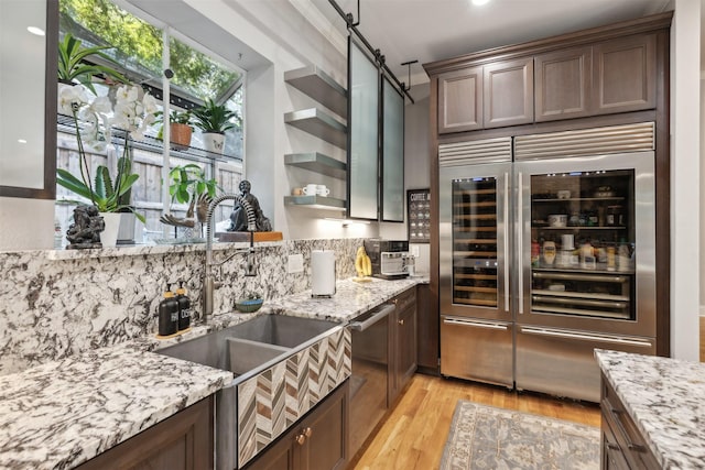 kitchen with light wood finished floors, tasteful backsplash, light stone counters, open shelves, and a sink