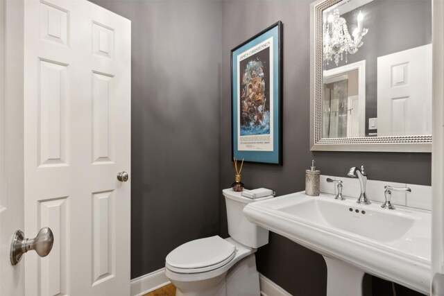 half bath featuring a chandelier, baseboards, a sink, and toilet