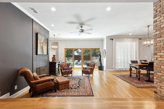 living room featuring light wood-type flooring, baseboards, ornamental molding, and ceiling fan with notable chandelier