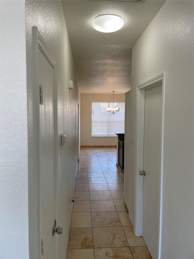 hallway with light tile patterned floors, a notable chandelier, baseboards, and a textured ceiling