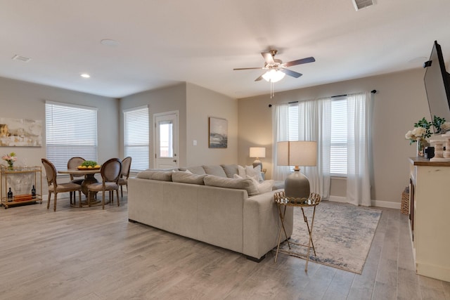 living area featuring baseboards, light wood-style flooring, visible vents, and a ceiling fan