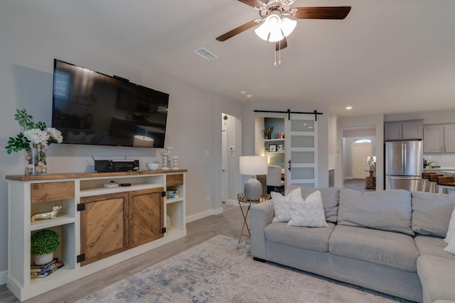 living room with visible vents, a barn door, a ceiling fan, wood finished floors, and baseboards