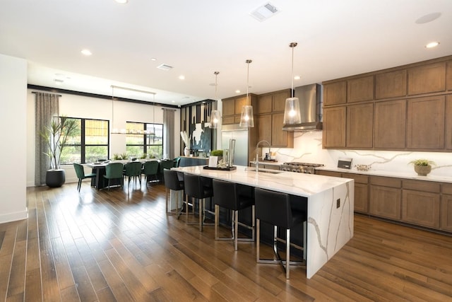 kitchen with visible vents, dark wood finished floors, a spacious island, wall chimney exhaust hood, and a sink