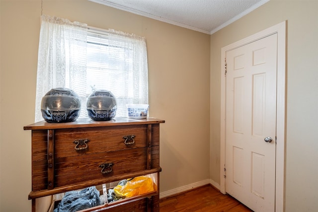 interior space with a textured ceiling, crown molding, wood finished floors, and baseboards